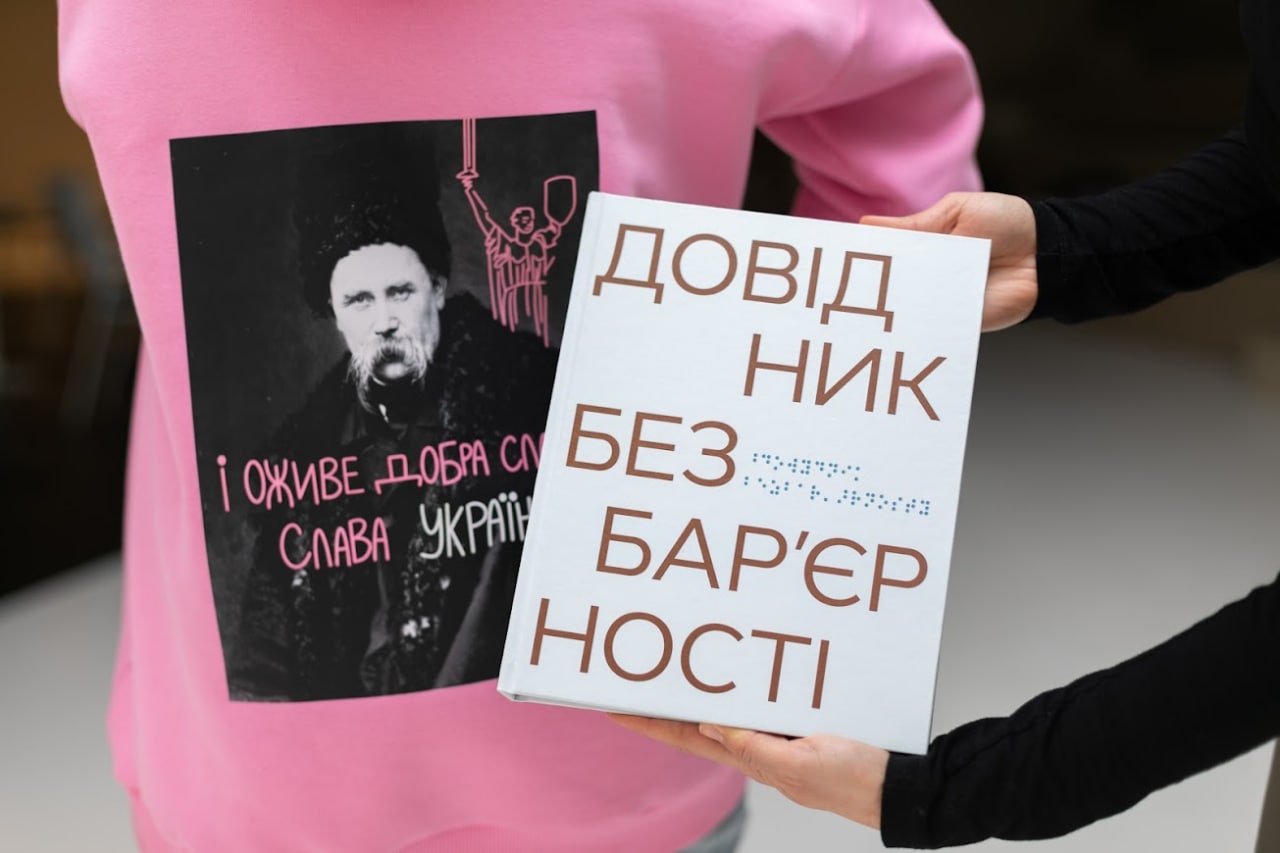 дівчина у рожевому худі тримає в руках книгу - Довідник безбар'єрності